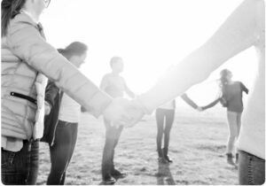 This is a black and white image of people holding hands in a circle with the sun in the background